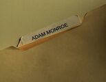 Bob porte un dossier intitulé « Adam Monroe ».